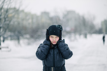 Fototapeta na wymiar girl covered her mouth with gloves. girl made a gesture, silence. child walks after school on street in a snowfall.