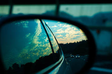 Ultimate roadtrip : car mirror picture of high speed highway road, cars, and nature in evening sky