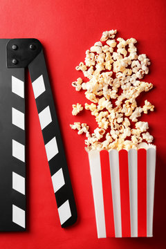 Paper bag with popcorn and movie clapper on color background