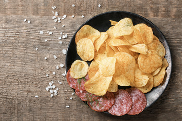 Plate with potato chips and salami on table