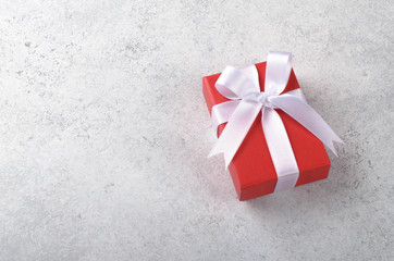 One red gift box with white bow lying on a light gray stone table, copy space