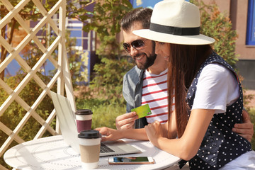 Fototapeta premium Young couple with laptop and credit card in open air cafe. Internet shopping concept