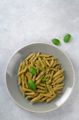 Pasta with homemade pesto sauce in a white plate on a light-blue stone slate background, vertical image, top view, copy space