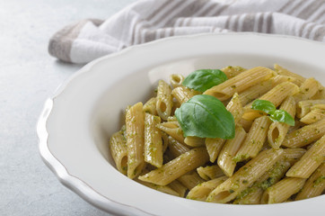Pasta with homemade pesto sauce in a white plate on a light-blue stone slate background, closeup