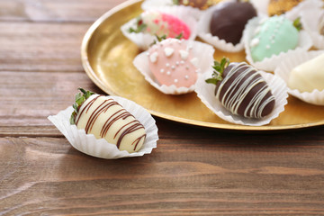 Plate with tasty glazed and chocolate dipped strawberries on wooden table