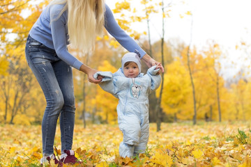 First steps of little kid in autumn park. Mother teaching her cute little son to walk.