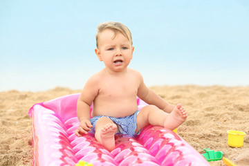 Cute baby boy sitting on inflatable mattress at beach