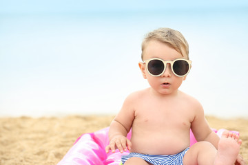 Cute baby boy sitting on inflatable mattress at beach