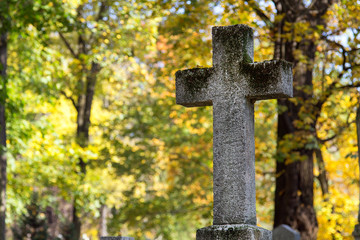 Stary kamienny krzyż na cmentarzu w otoczeniu jesiennych drzew. Symbol chrześcijaństwa - obrazy, fototapety, plakaty