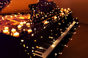 Vintage piano with Christmas lights and candles in dark room