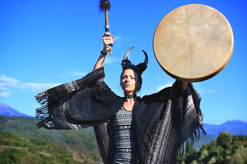 Tribal woman with horns playing a Buffalo drum on the mountain