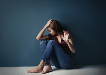 Battered young woman sitting near blue wall