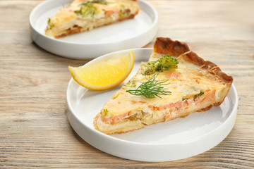 Plate with piece of tasty salmon quiche on table
