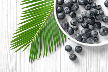 Plate with fresh acai berries and palm leaf on wooden table