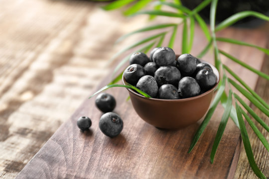 Bowl with fresh acai berries on wooden table, closeup