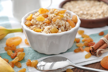 Tasty oatmeal with raisins in bowl on table