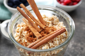 Tasty oatmeal with cinnamon sticks in glass, close up