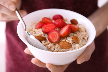 Sporty woman holding spoon and bowl with nutritious oatmeal, close up