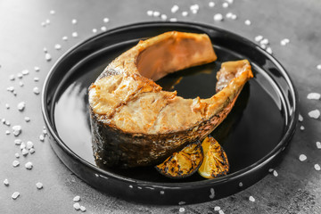 Black plate with fried fish steak on grey background