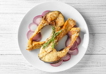 Ceramic plate with fried fish steaks on wooden background