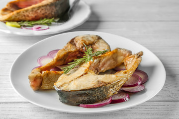 Ceramic plate with fried fish steaks on wooden background