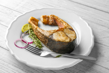Ceramic plate with fried fish steak on wooden background