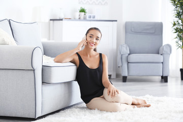 Beautiful young woman speaking by mobile phone at home