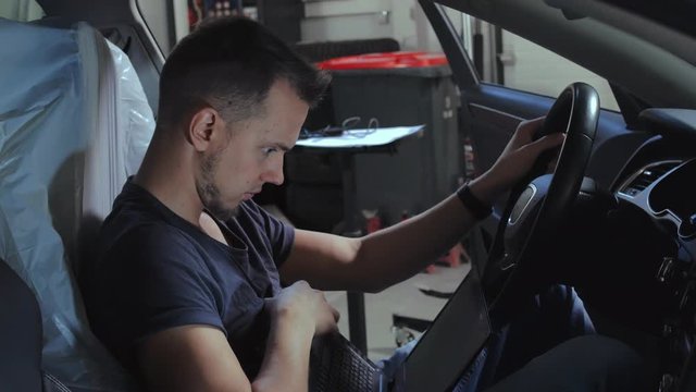 Car service man making computer diagnostics engine sitting inside the car