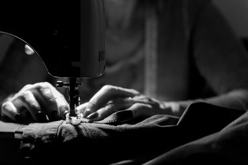 Close up on sewing machine and seamstress' hand while she is working. Black and white