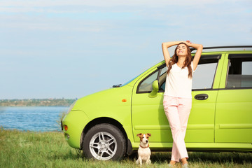 Naklejka premium Beautiful young woman with cute dog standing near car