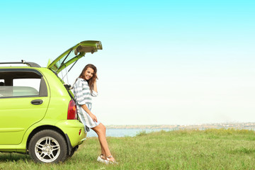 Beautiful young woman sitting in car trunk outdoors