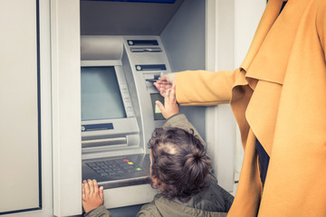 Little girl withdrawing money form ATM with help of mother.