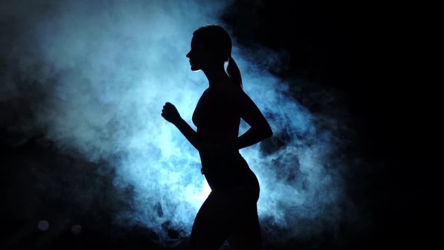 Lady running on a smoky spotlight on black background. Silhouette. Slow motion