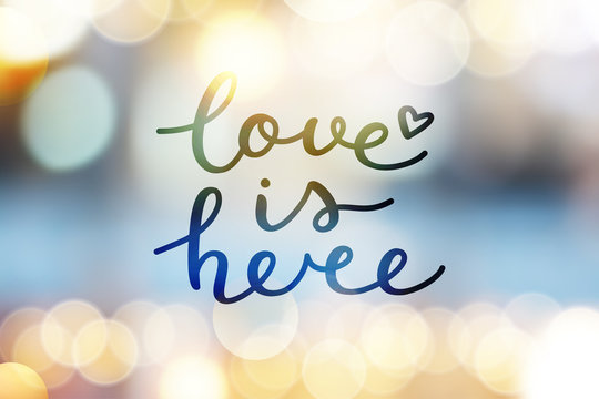 love is here lettering, vector handwritten text on blurred lights