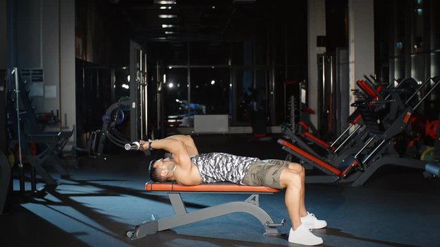 Attractive male bodybuilder doing chest workout and press exercise lifting dumbbells in gym