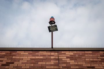 Isolated external lamp. Halogen lamp on exterior of building facade. Rooftop with hanging flood light. PIgeon spikes on roof. Architectureal detail. Abstract colors.