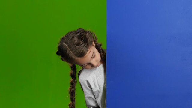 Child looks out from behind the blue board and laughs. Green screen