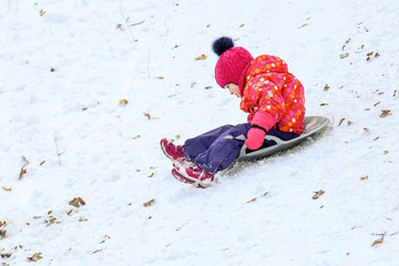 Little cute caucasian girl having fun sledding in a forest or city park on a brighht sunny day. Winter children activity concept