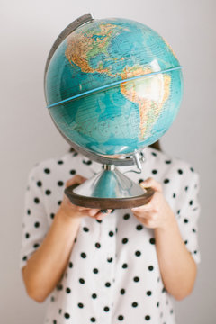 Woman covering her face with a globe against gray background
