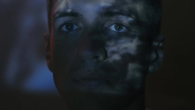 close-up of young man watching a movie at night. Reflection on the face