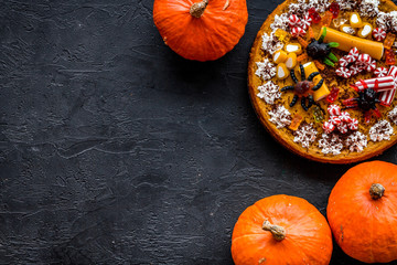 Homemade pie for halloween decorated gummy spiders among pumpkins on black background top view copyspace