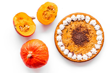 Obraz na płótnie Canvas Homemade pumpkin pie decorated whipped cream and chocolate near pumpkins on white background top view