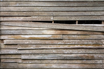 The old wooden wall house is ruined and one piece of old wood is falling down with can see the inner darkness as texture and background