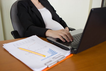 Close-up of pregnant woman belly  with laptop computer on wooden table ,blank screen laptop computer.