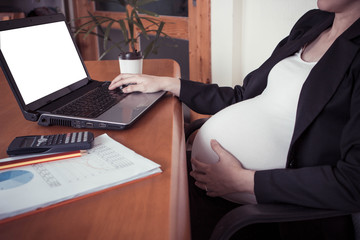 Close-up of pregnant woman belly  with laptop computer on wooden table ,blank screen laptop computer.