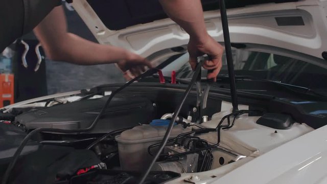 Mechanic man measuring voltage on car battery in auto service. Car servicing