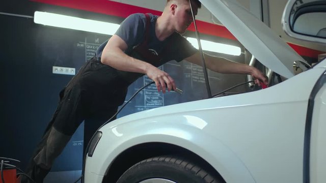 Auto service worker checking voltage on car battery. Car service station