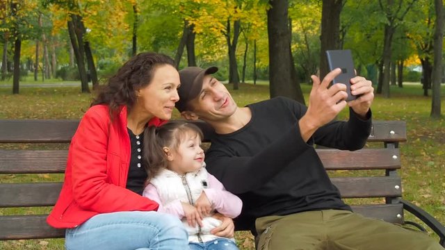 Happy family in the park with a tablet. The father takes pictures of the family from the tablet.