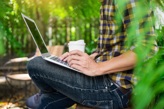 man on week-end working on laptop computer outdoor in a park garden during a sunny summer day.