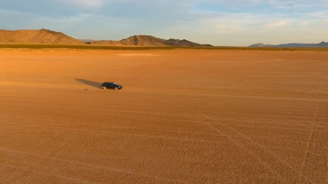 Aerial tracking shot of a car moving across a dry lake in the desert